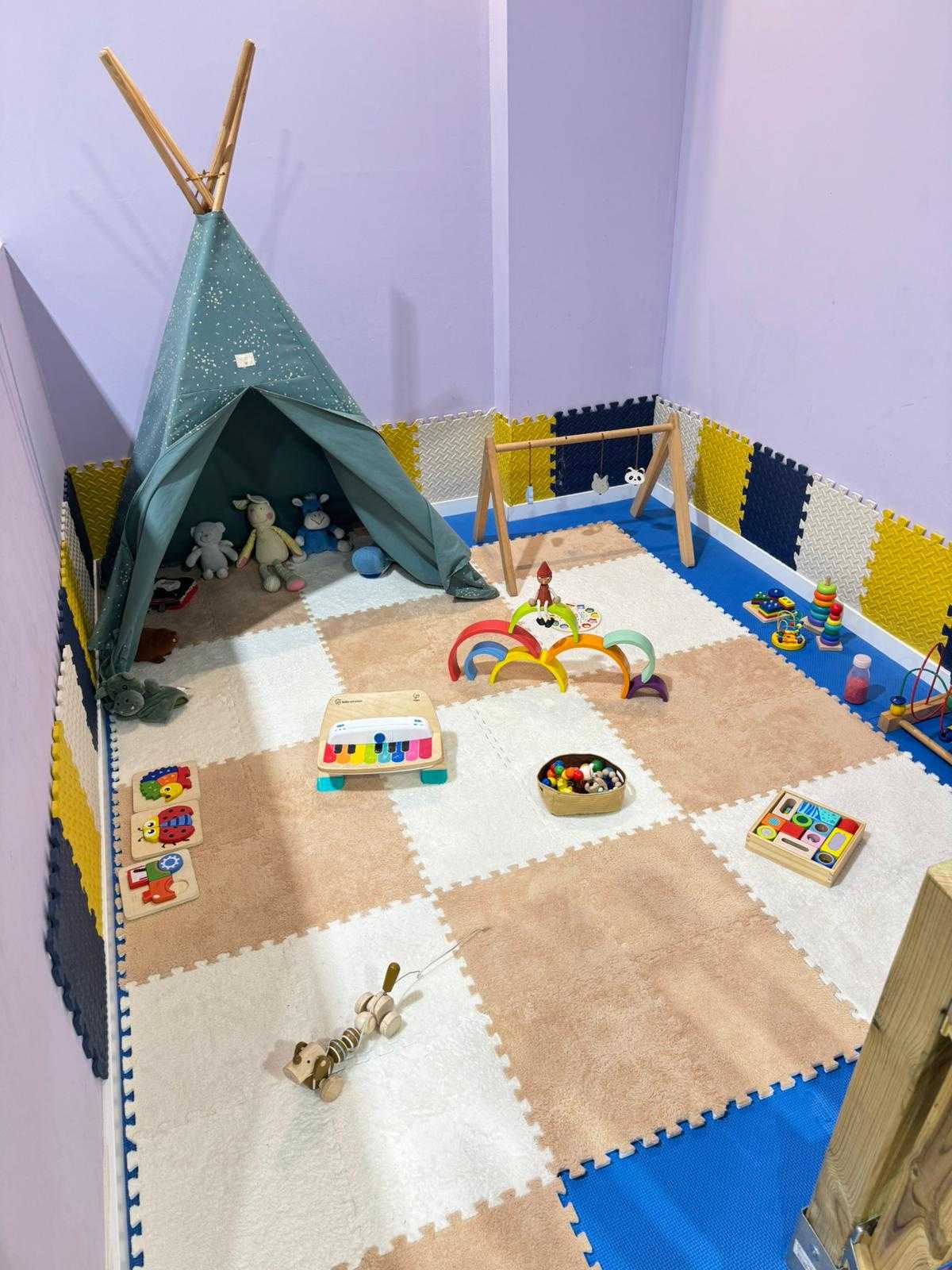 Un rincón de juegos acogedor, lleno de juguetes coloridos y un tipi verde azulado, perfecto para la imaginación infantil.